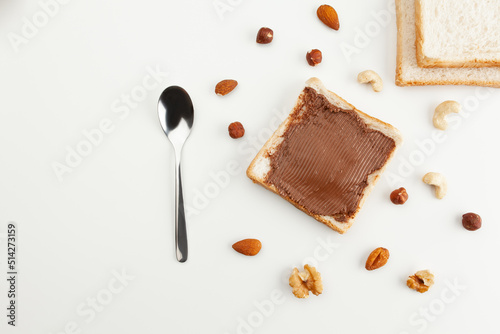 Square bread for toast with chocolate spread. Nuts, spoon, slices of bread and a sandwich with chocolate spread on a white table.