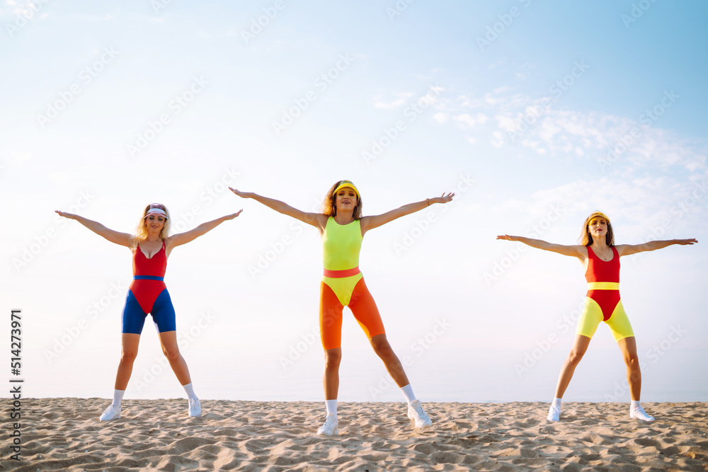 Beautiful women in swimsuits are dancing on the beach. Three woman are training in the morning. Fitness, training, aerobics and people concept. Active sport.