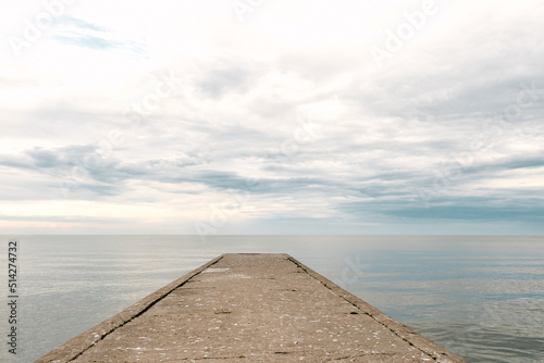 Empty concrete pier to the sea with dramatic sky and calm water, abandoned industrial jetty © BOOCYS