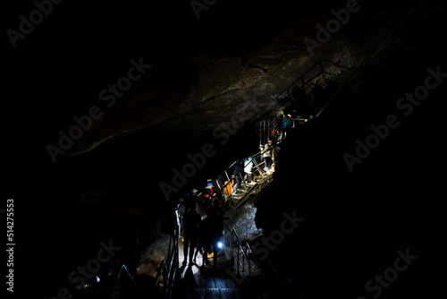 Fototapeta Naklejka Na Ścianę i Meble -  A group of people climb the stairs in complete darkness, the light from the lantern illuminates the road up, an organized group of tourists visit the cave, speleologists explore the grotto.