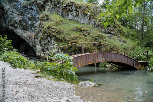 The ancient rock entrance to the cave is a wooden bridge over the river  outdoor recreation  beautiful landscape  park area in the forest  mountain stream.