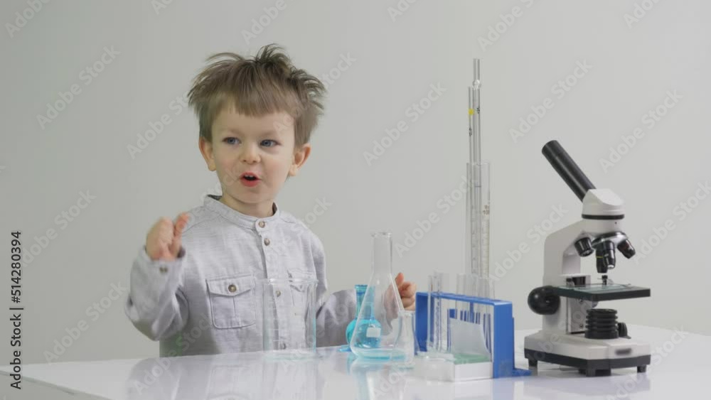 Cute little boy playing the scientist in the research laboratory, near microscope and glassware, showing thumb up OK sign and deny NOK sign Cute little boy playing the scientist in the research laboratory, near microscope and glassware, showing thumb up OK sign and deny NOK sign