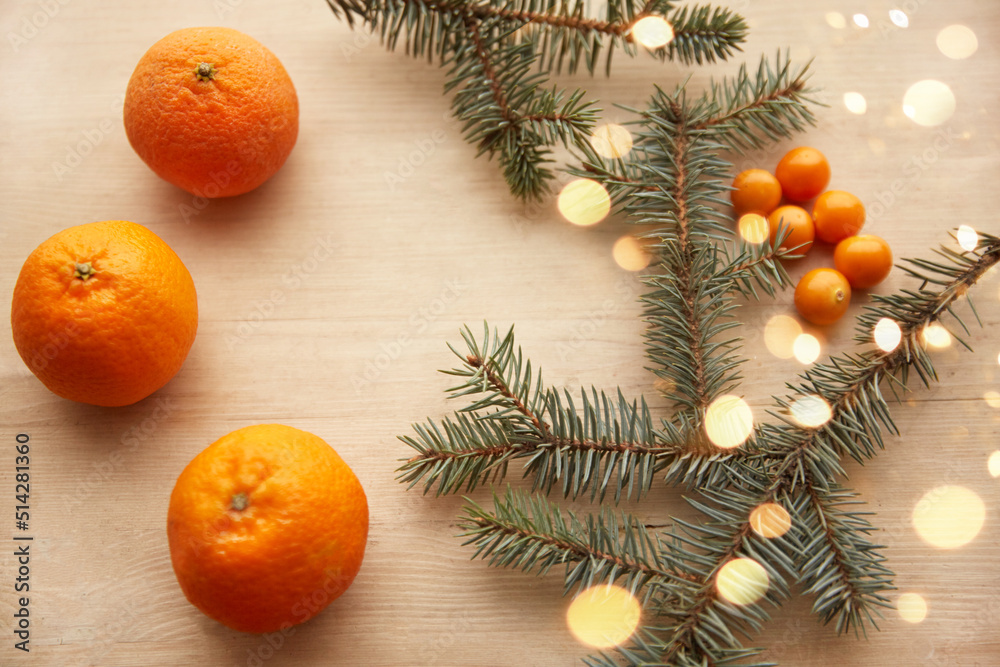 Fir branches with garlands on a light wooden background, decorated with tangerines and berries. View from above. Christmas concept. High quality photo Fir branches with garlands on a light wooden background, decorated with tangerines and berries. View from above. Christmas concept. High quality photo