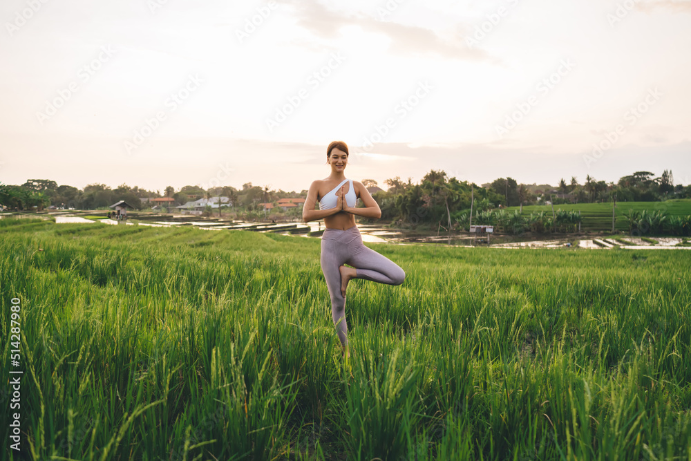 Carefree woman with perfect body figure practicing yoga during summer vacations for recreation in Indonesia, happy female standing in tree namaste pose spending morning at rice fields of Bali Carefree woman with perfect body figure practicing yoga during summer vacations for recreation in Indonesia, happy female standing in tree namaste pose spending morning at rice fields of Bali