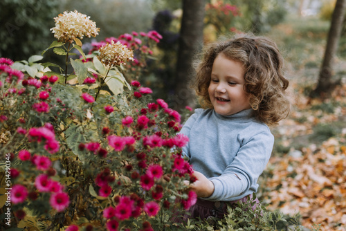 adorable curly little girl in blue shirt in park with flowers at fall time, autumn, health, card, banner