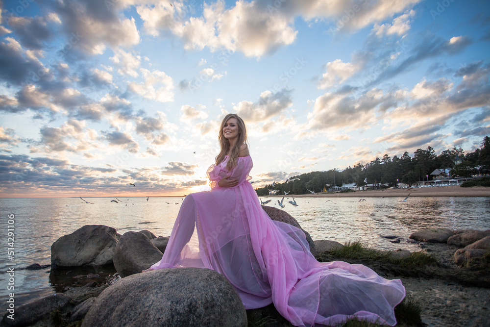 Beautiful young stylish woman in elegant pink dress outdoors at sunset sky clouds background Beautiful young stylish woman in elegant pink dress outdoors at sunset sky clouds background