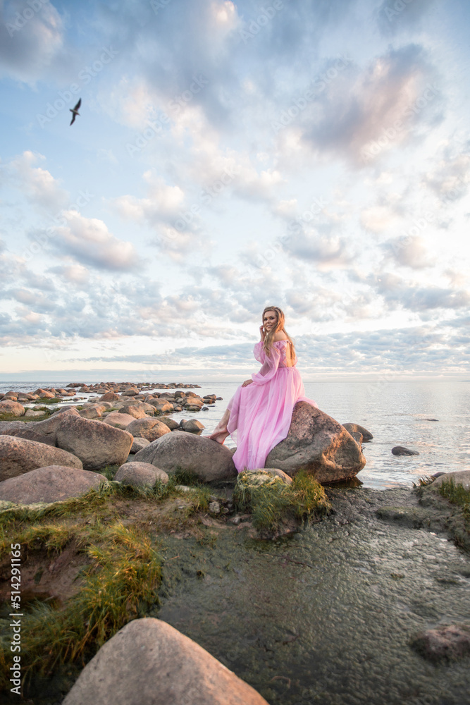 Woman in a long pink dress on the beach, sunset