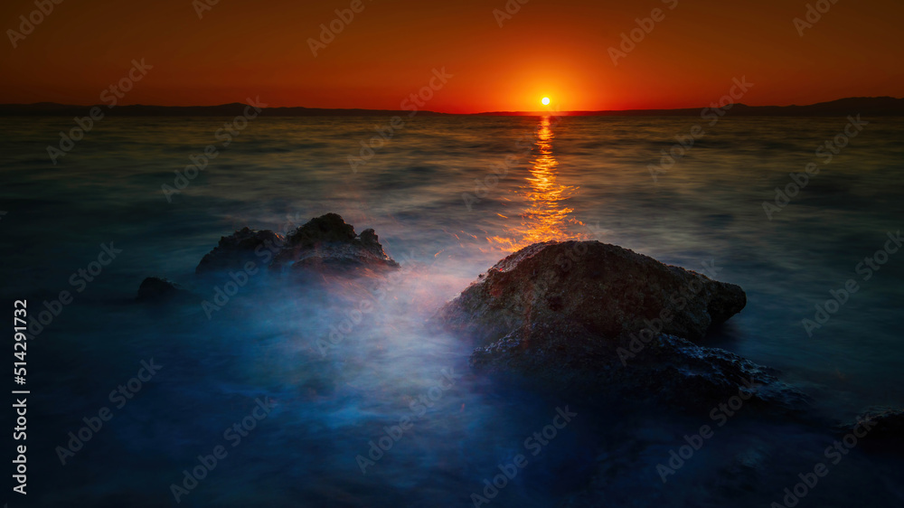 Widok skał oblewanych przez morze o wschodzie słońca przy kolorowym niebie - obrazy, fototapety, plakaty 