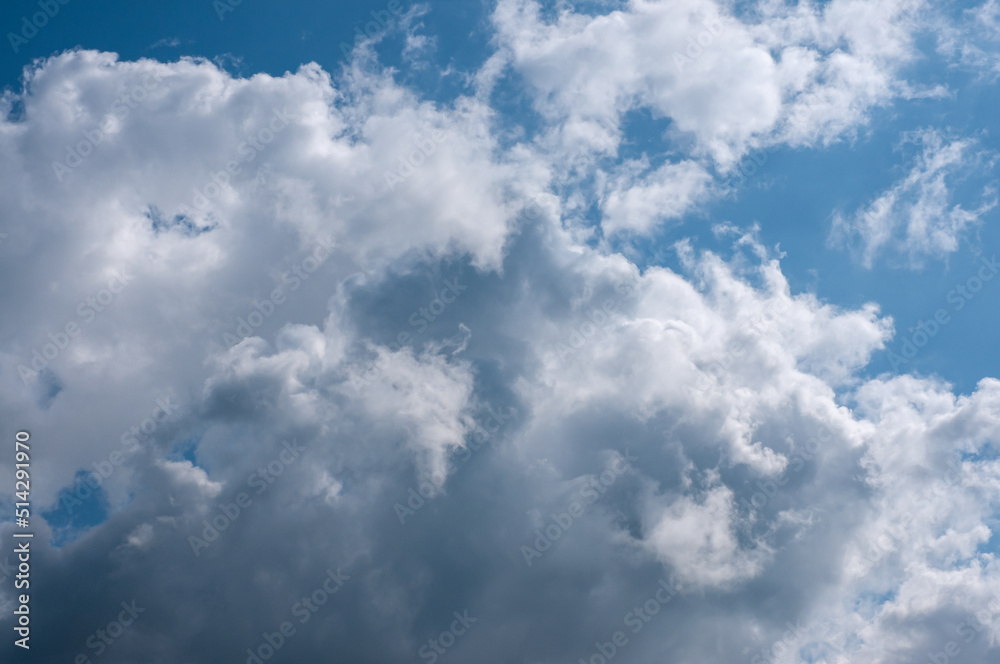 Cumulus gray-white clouds illuminated by rays of sun against background of blue sky on hot summer day. Sky is in large clouds.