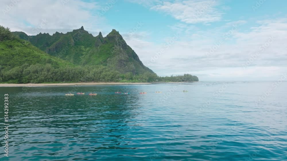 Cinematic aerial view group of tourists in colorful kayaks rowing in blue open waters of Pacific ocean. Kayakers on green mountain motion background, Napali park coast kayak tour, Kauai island Hawaii Cinematic aerial view group of tourists in colorful kayaks rowing in blue open waters of Pacific ocean. Kayakers on green mountain motion background, Napali park coast kayak tour, Kauai island Hawaii