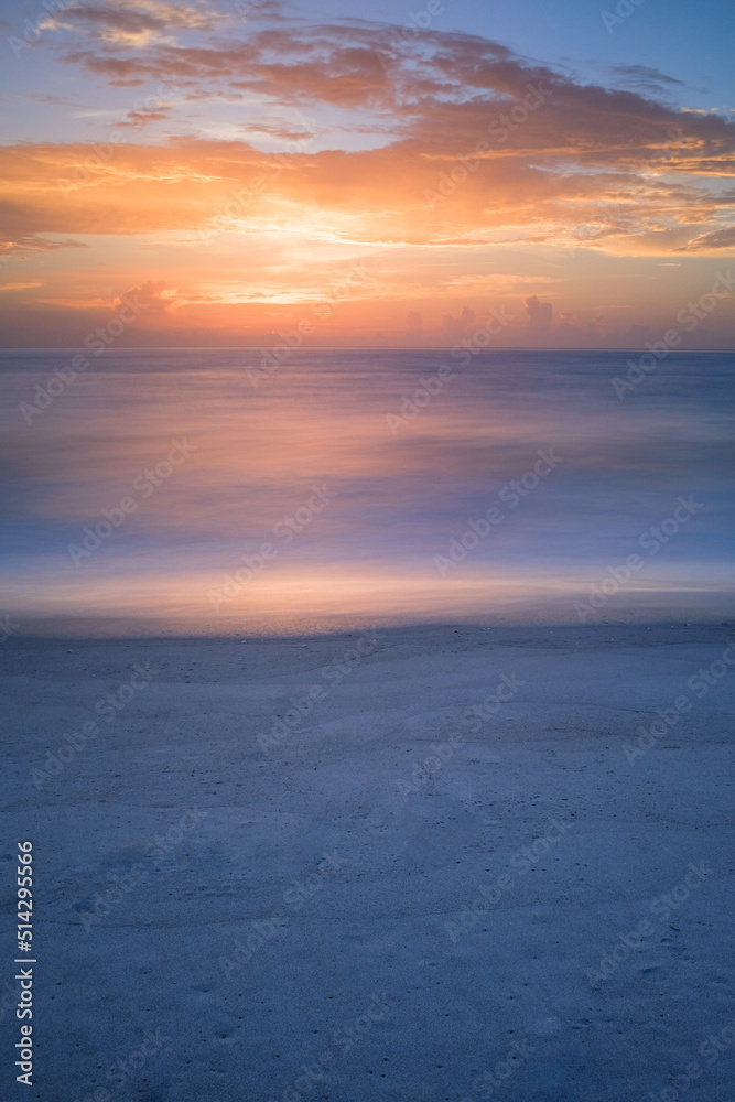 a long exposure of a calm sea reflecting a sunset with a sandy beach foreground