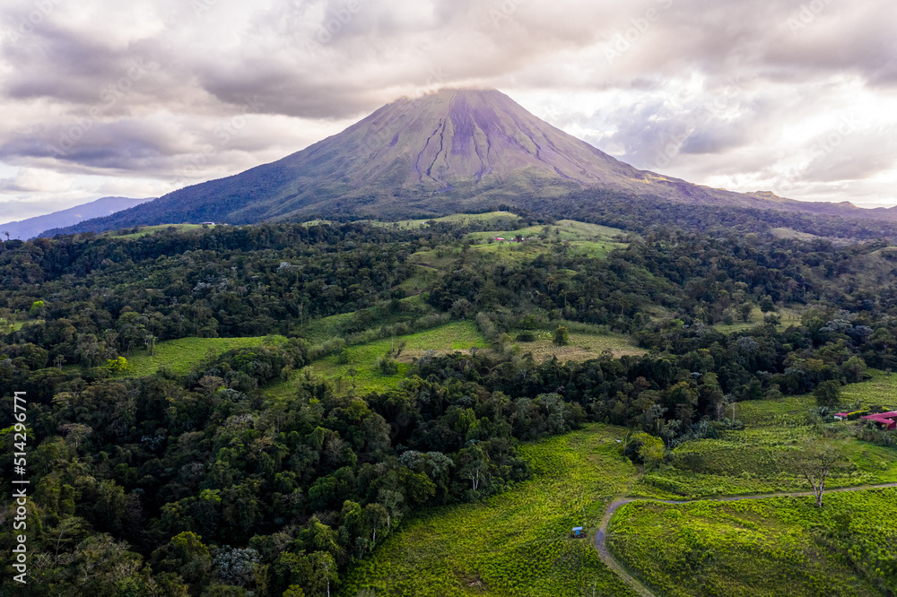Arenal Volcano rises into a cloudy sky with farmland and jungle Arenal Volcano rises into a cloudy sky with farmland and jungle