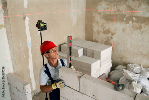 Fotografia Bricklayer or mason lays bricks to construct wall of autoclaved aerated concrete blocks