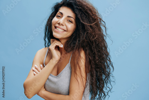 Overjoyed gorgeous curly Latin woman laugh at camera isolated blue background, hold hand near jaw,and smiling to you. Good offer for fashion and cosmetics brands. Copy space, free place for ad
