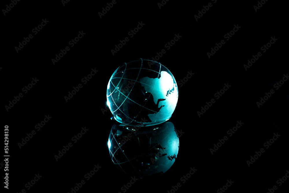 Green glass globe on a black background. Planet Earth close-up with reflection in water. Crystal sphere in the form of a globe in water. Glass ball with a map on a black background.
