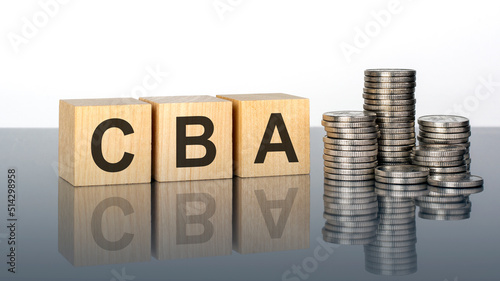 CBA - text on wooden cubes on a cold grey light background with stacks coins