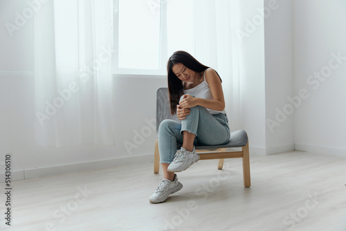 Cramp Broken Toe Broken Bone in Leg. Tormented suffering tanned beautiful young Asian woman touch leg at home interior living room. Injuries Poor health Illness concept. Cool offer Banner