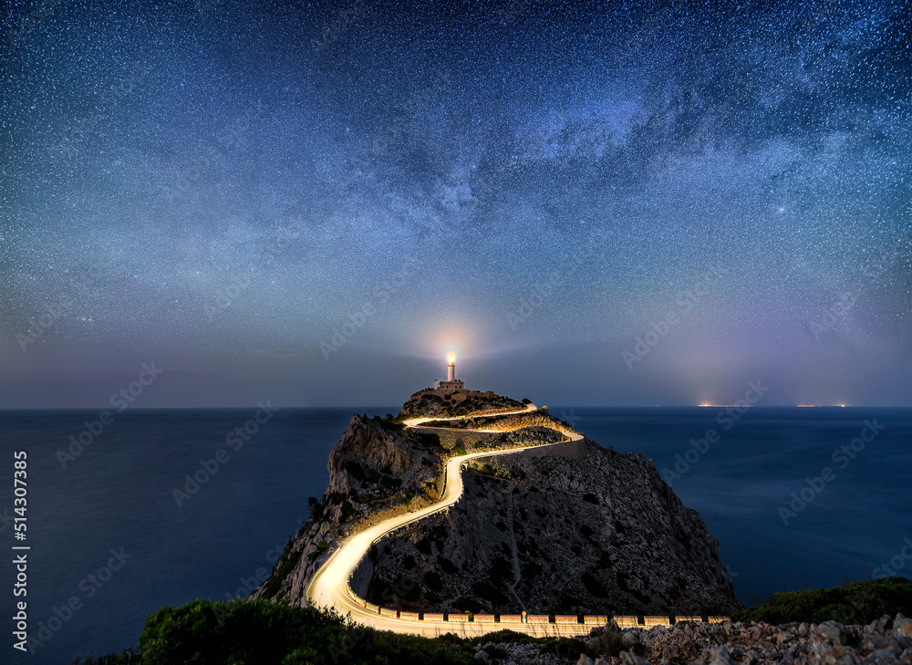 Night time image with milky way stars and illuminated road with light trails at the Far de Formentor lighthouse on Mallorca, Spain - obrazy, fototapety, plakaty 