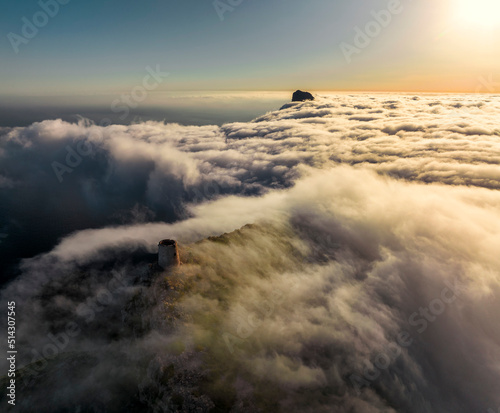 Aerial image of low clouds at sunrise at the historic Albercutx watchtower in golden light at Mallorca, Spain photo