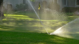 Multiple sprinklers water a green on a golf course early in the morning.