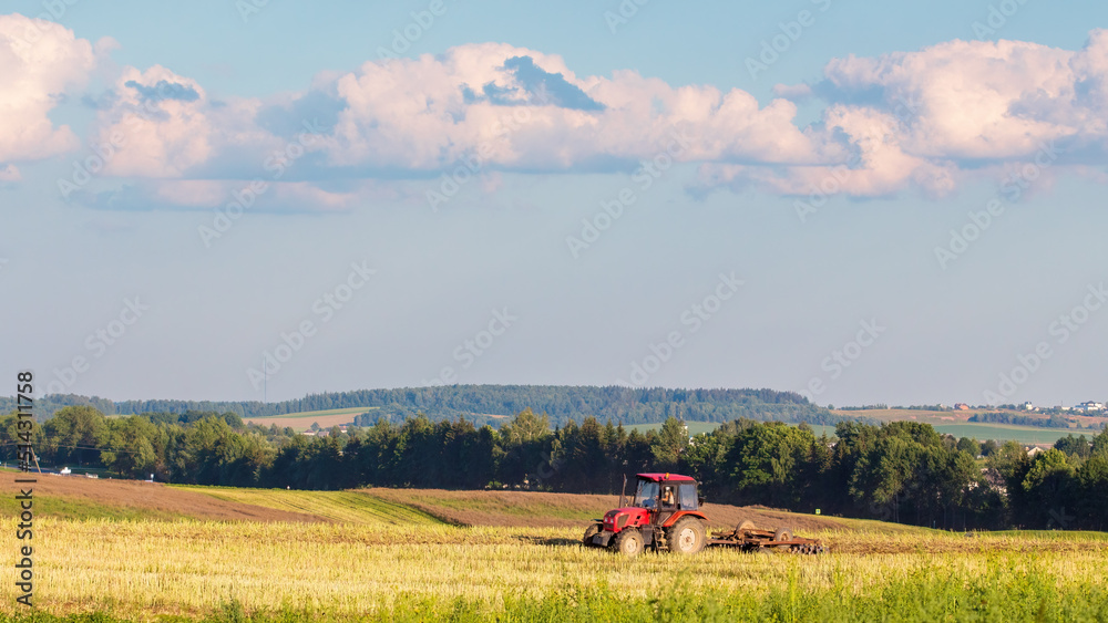 Panorama of harvested agricultural field and tractor plowing land. Endless expanses
