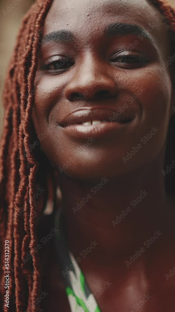 VERTICAL VIDEO: Close-up of beautiful woman with African braids raising her head and looking at the camera with smile on the building background. Close-up Slow Motion VERTICAL VIDEO: Close-up of beautiful woman with African braids raising her head and looking at the camera with smile on the building background. Close-up Slow Motion