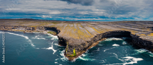 View on rough stone coast line of Aran island, county Galway, Ireland. High stone cliff. Blue cloudy sky and ocean surface. Aerial view. Stunning Irish nature landscape.