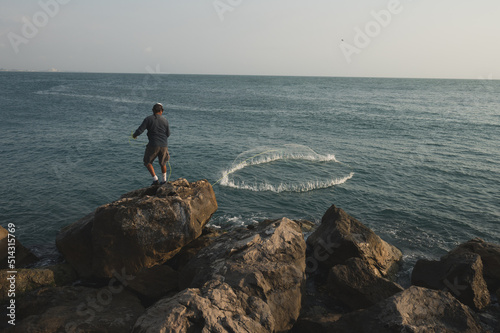 Fisherman throwing his net in the morning towards the sea from the breaking waves photo
