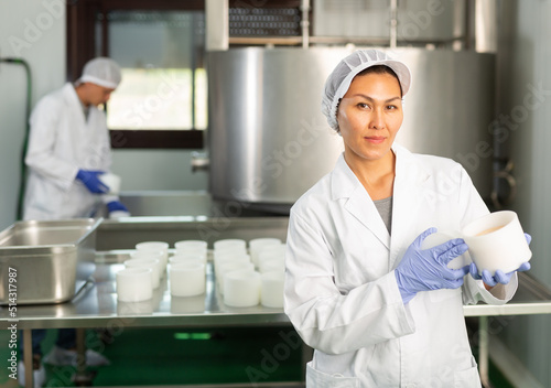 Woman wearing uniform showing cottage cheese production process on dairy factory