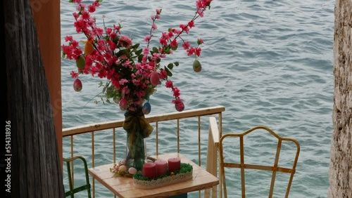 An elegant forged metal table with a bouquet of flowers and symbolic Easter eggs against the backdrop of sea waves. Eve of Catholic Easter. Spring day. Croatia, Istria, Rovinj, circa April 2022