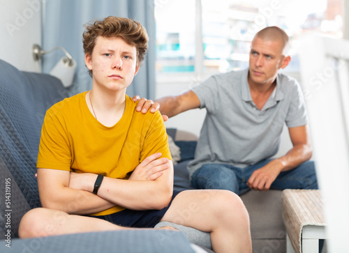 Portrait of father calming upset teenage son after quarrel