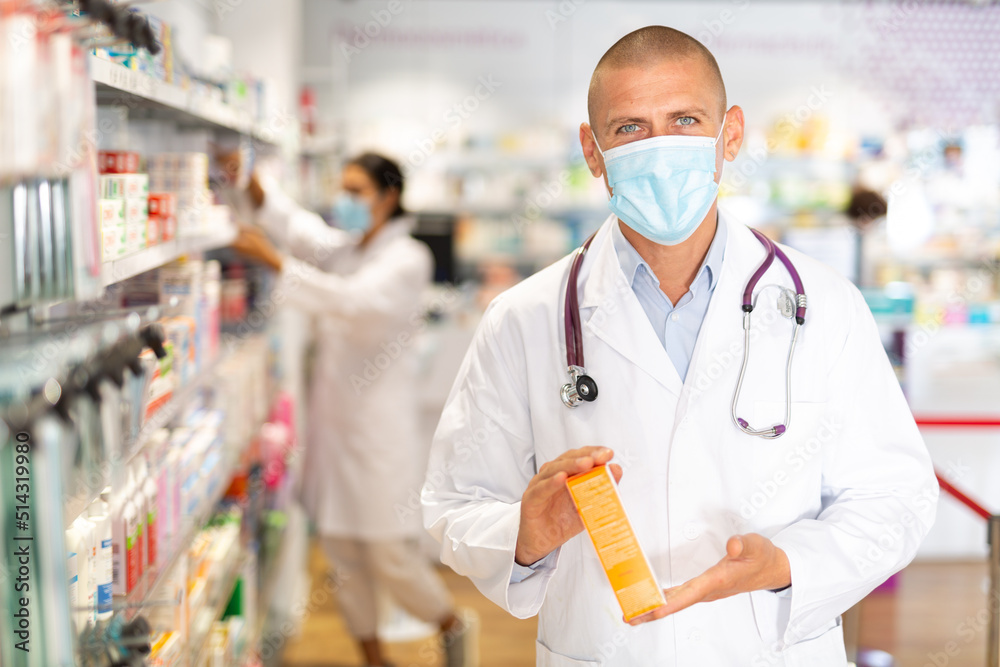Male pharmacist in medical mask offers medicine while standing in the trading floor of a pharmacy