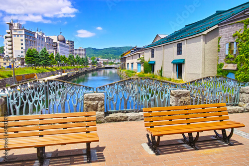 新緑の北海道小樽市、浅草橋街園から見る快晴の小樽運河の倉庫群とベンチの風景
