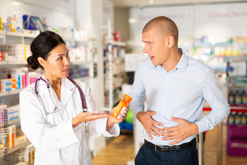 Man complains to a pharmacist about a sore belly. Help in choosing a medicine in a pharmacy