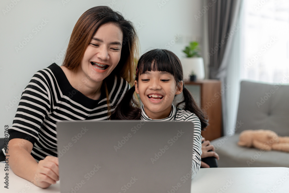 Asian little young girl kid learning online class at home with mother. Preschool child use laptop computer do homework, homeschool from school teacher by digital remote internet with support from mom. Asian little young girl kid learning online class at home with mother. Preschool child use laptop computer do homework, homeschool from school teacher by digital remote internet with support from mom.