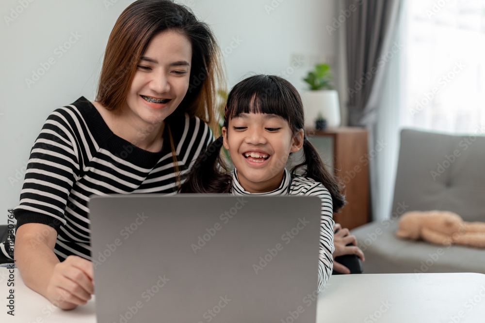 Asian little young girl kid learning online class at home with mother. Preschool child use laptop computer do homework, homeschool from school teacher by digital remote internet with support from mom. Asian little young girl kid learning online class at home with mother. Preschool child use laptop computer do homework, homeschool from school teacher by digital remote internet with support from mom.