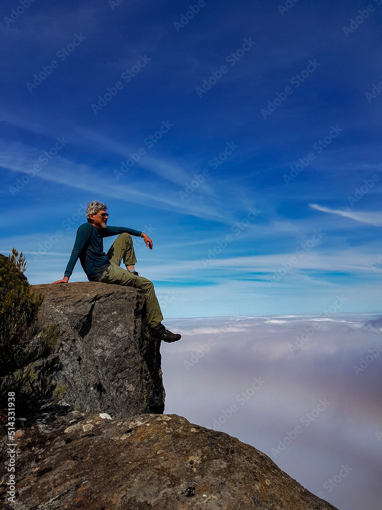 Man sitting on top of a rock contemplating mountains covered by clouds in Serra do Caparaó