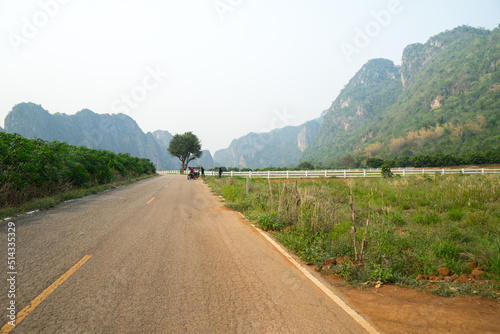 Along road with white concrete fence around the agriculture farm or ranching near the complicated mountain with road and sunlight background at the Ban Rai ,Uthai Thani, Thailand.
