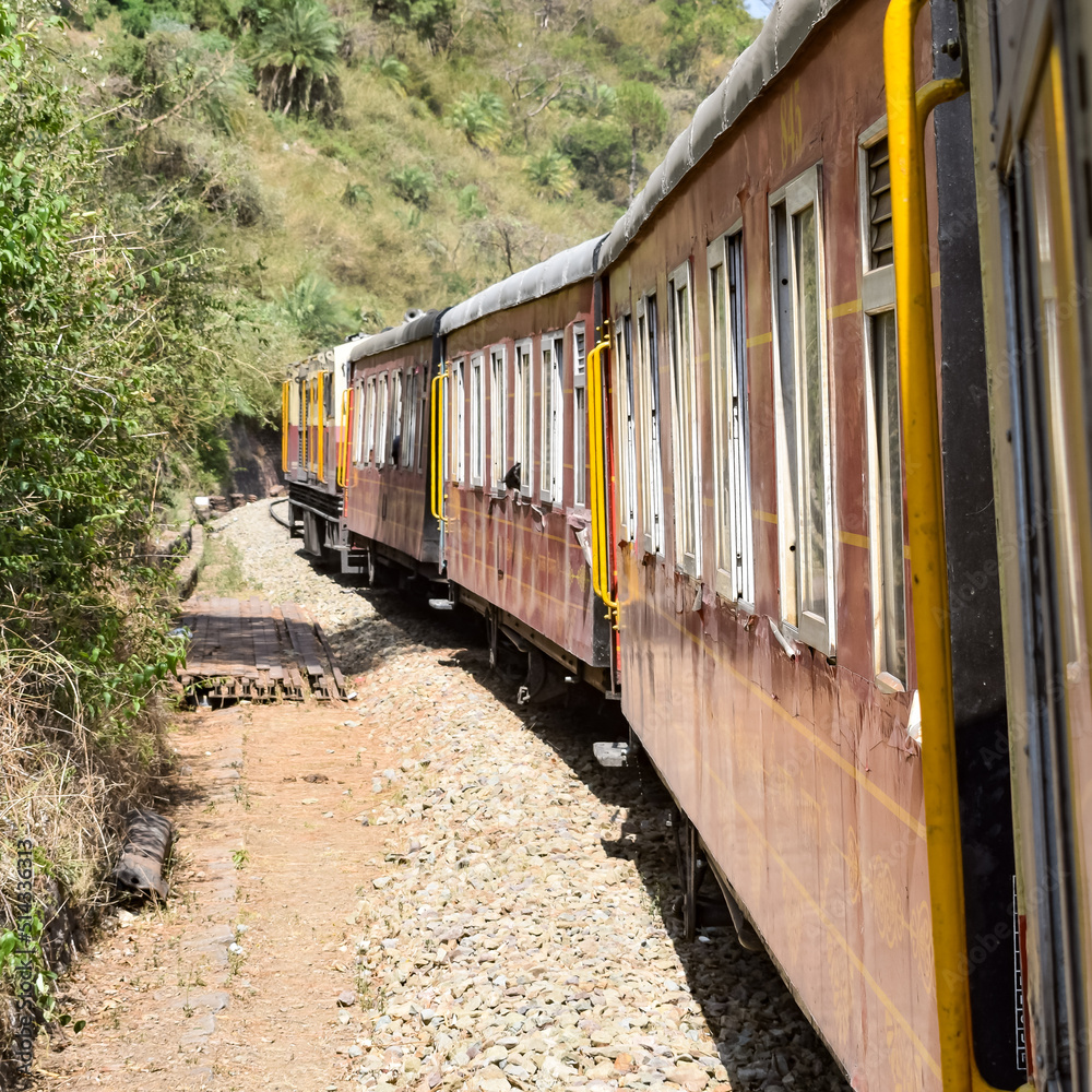 Obraz premium Toy Train moving on mountain slopes, beautiful view, one side mountain, one side valley moving on railway to the hill, among green natural forest. Toy train from Kalka to Shimla in India