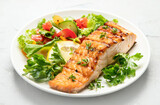 Salmon steak with vegetables and fries on light background.