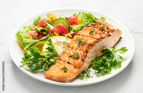 Salmon steak with vegetables and fries on light background.