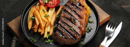 Striploin beef steak with french fries on dark background. photo