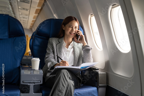 Young attractive and successful business asian woman talking on the phone and working while sitting in the chair of his private business plane