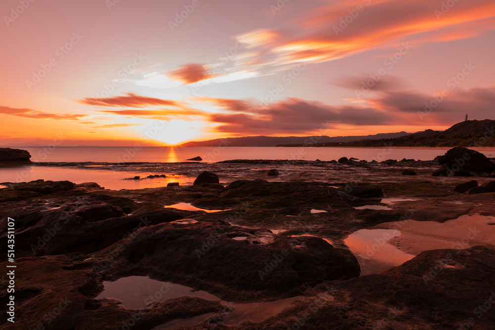 Amazing sunrise at seashore, sea puddles between coastal rocks, dramatic colorful sky.