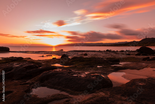 Amazing sunrise at seashore, sea puddles between coastal rocks, dramatic colorful sky.