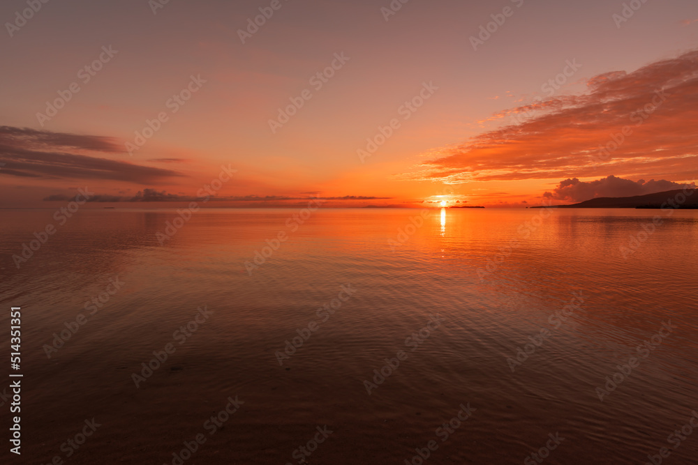 Vibrant sunrise in red shades at a tropical beach, soft waves.