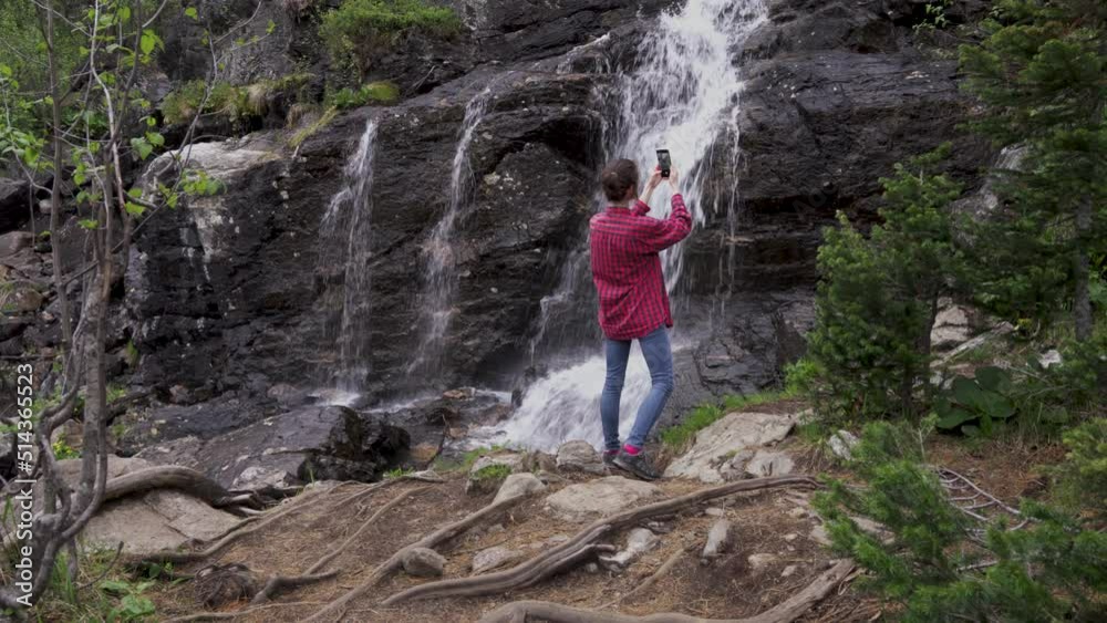 Young girl tourist with phone takes pictures of waterfall in forest Young girl tourist with phone takes pictures of waterfall in forest