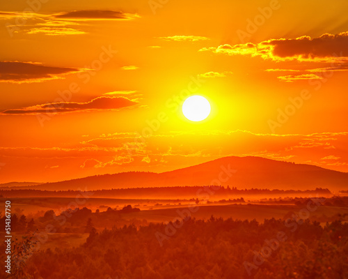The setting sun in the sky over the wooded hills