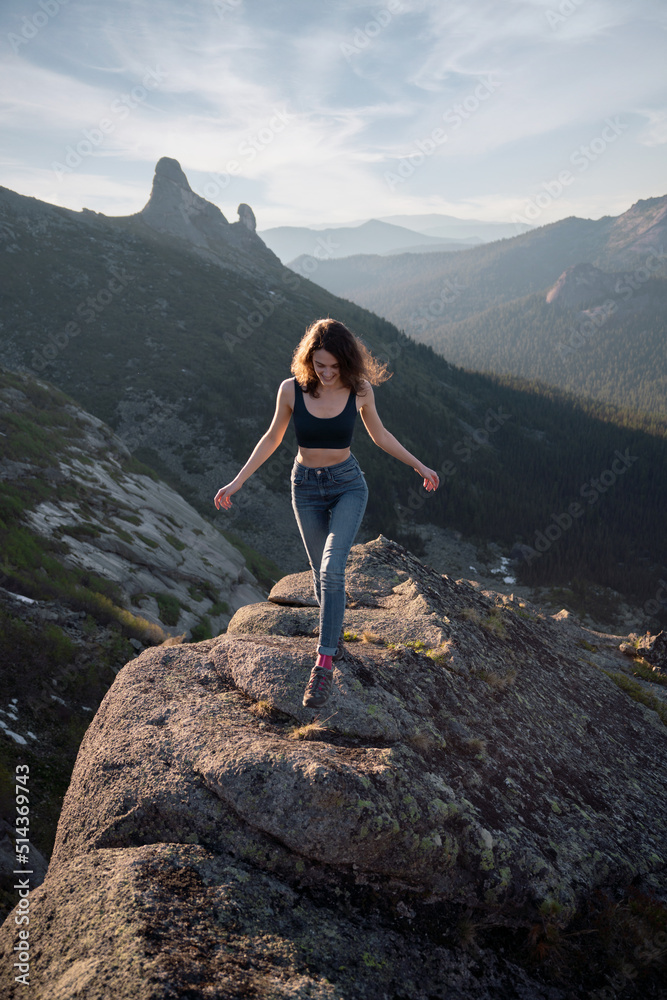 Young girl in sportswear walks along rock in mountains