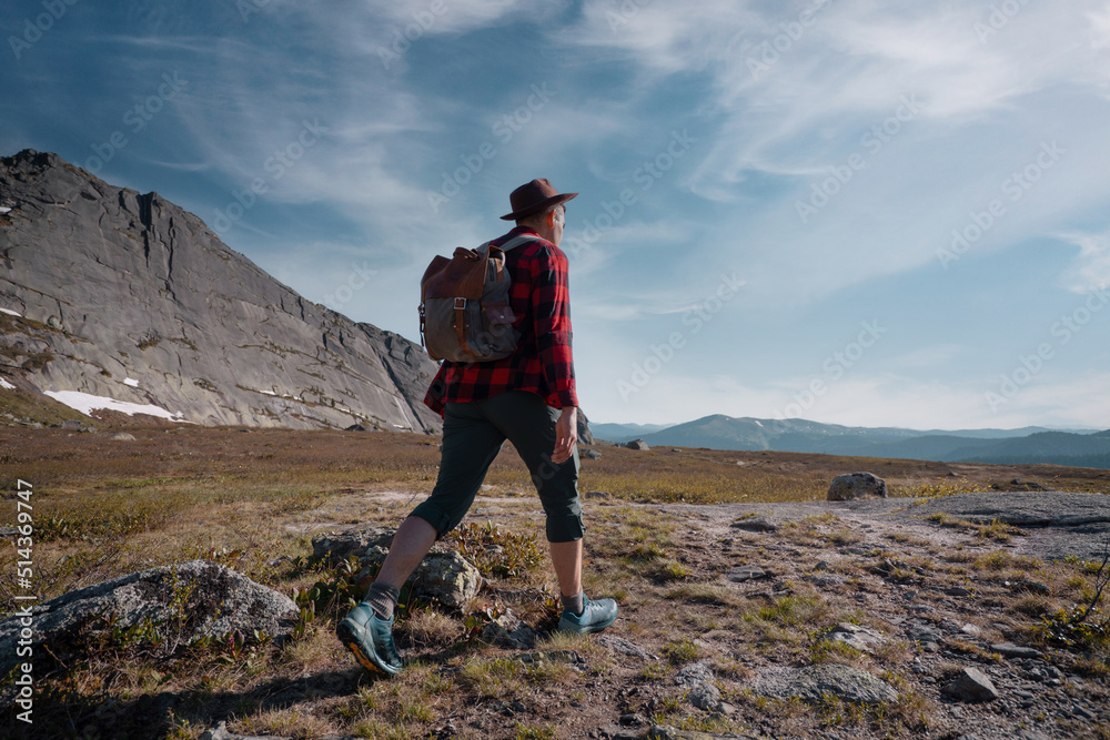Obraz premium Young traveler tourist dressed as hipster with backpack walks in mountains